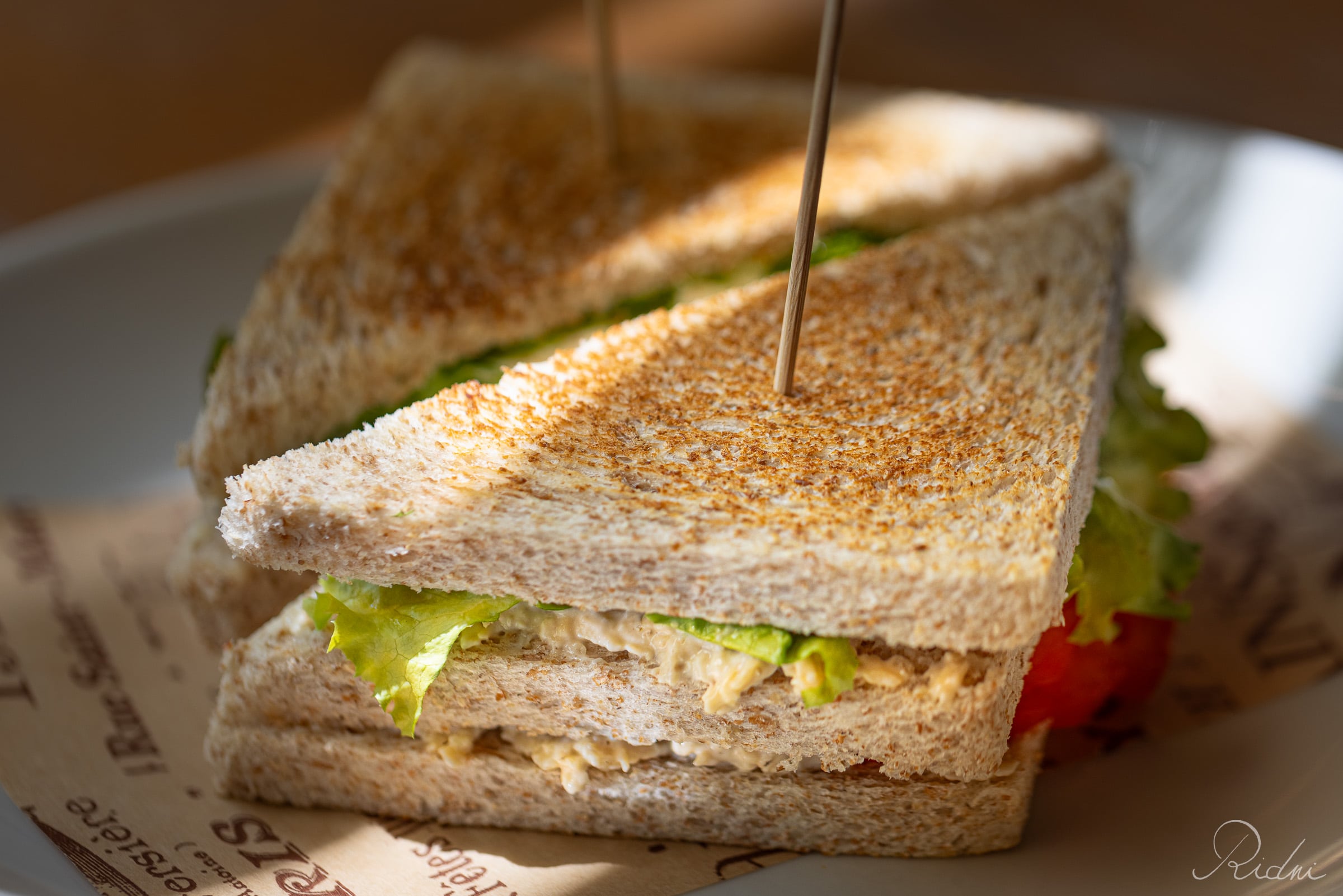 A close-up of a toasted club sandwich at bar Zona in lignano, friuli, featuring fresh lettuce and golden bread under warm natural light.