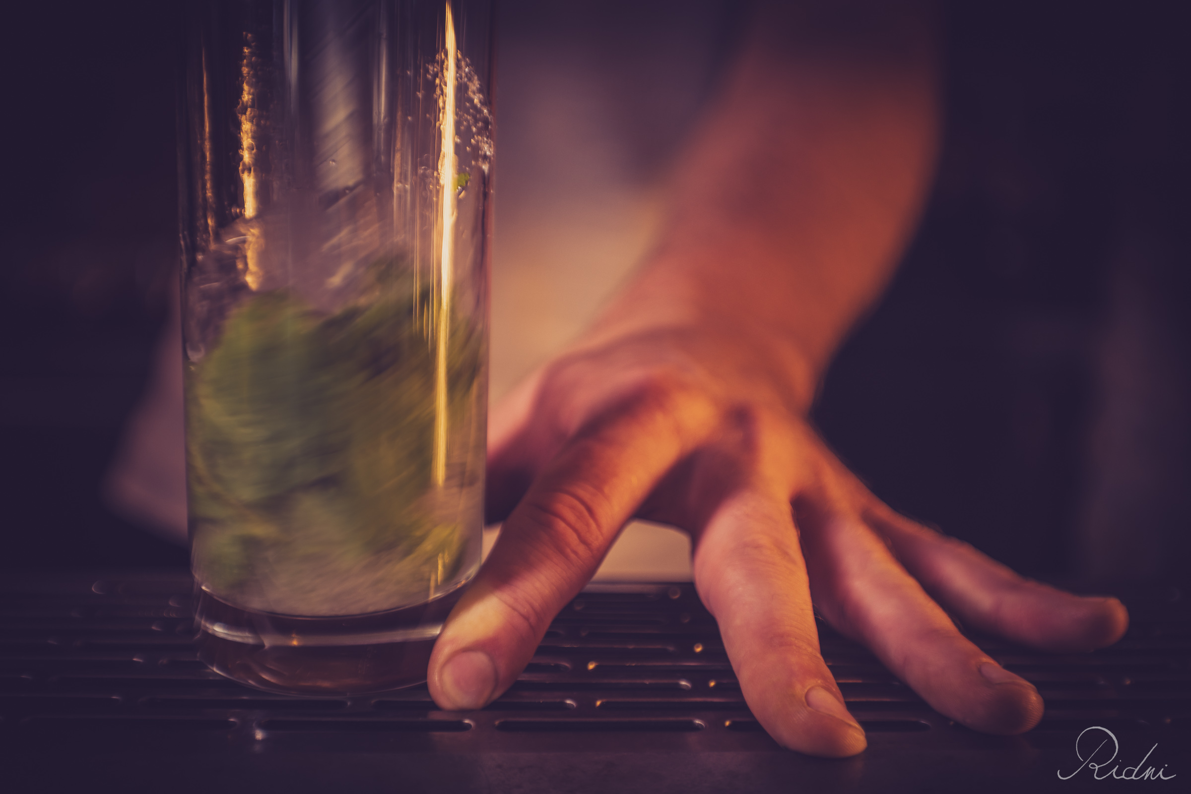A hand rests on the counter of bar Zona in lignano, friuli, next to a tall glass filled with fresh mint leaves for a cocktail.