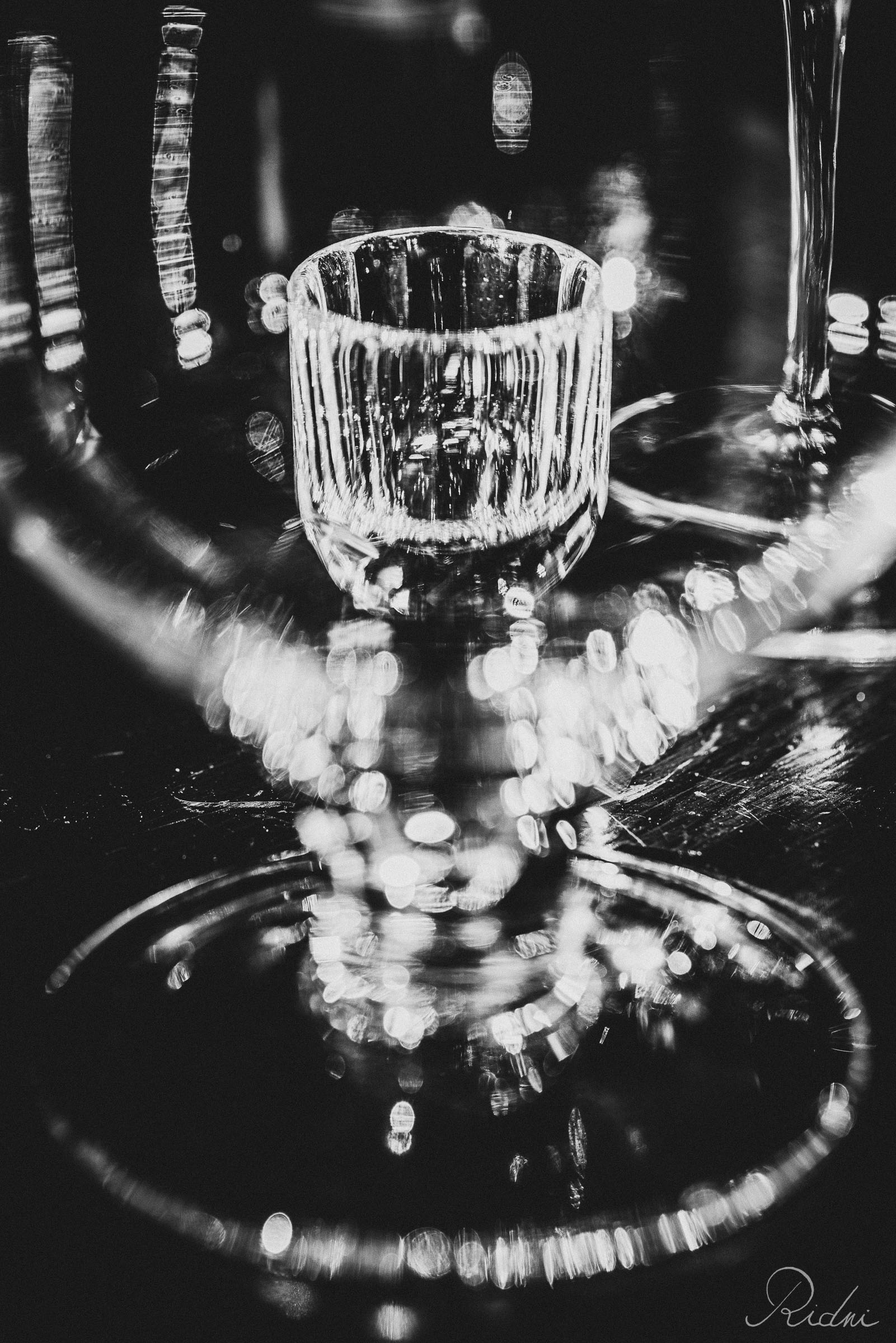 Detailed black and white view of glassware at bar Zona in lignano, friuli, showcasing shimmering light reflections and bokeh.
