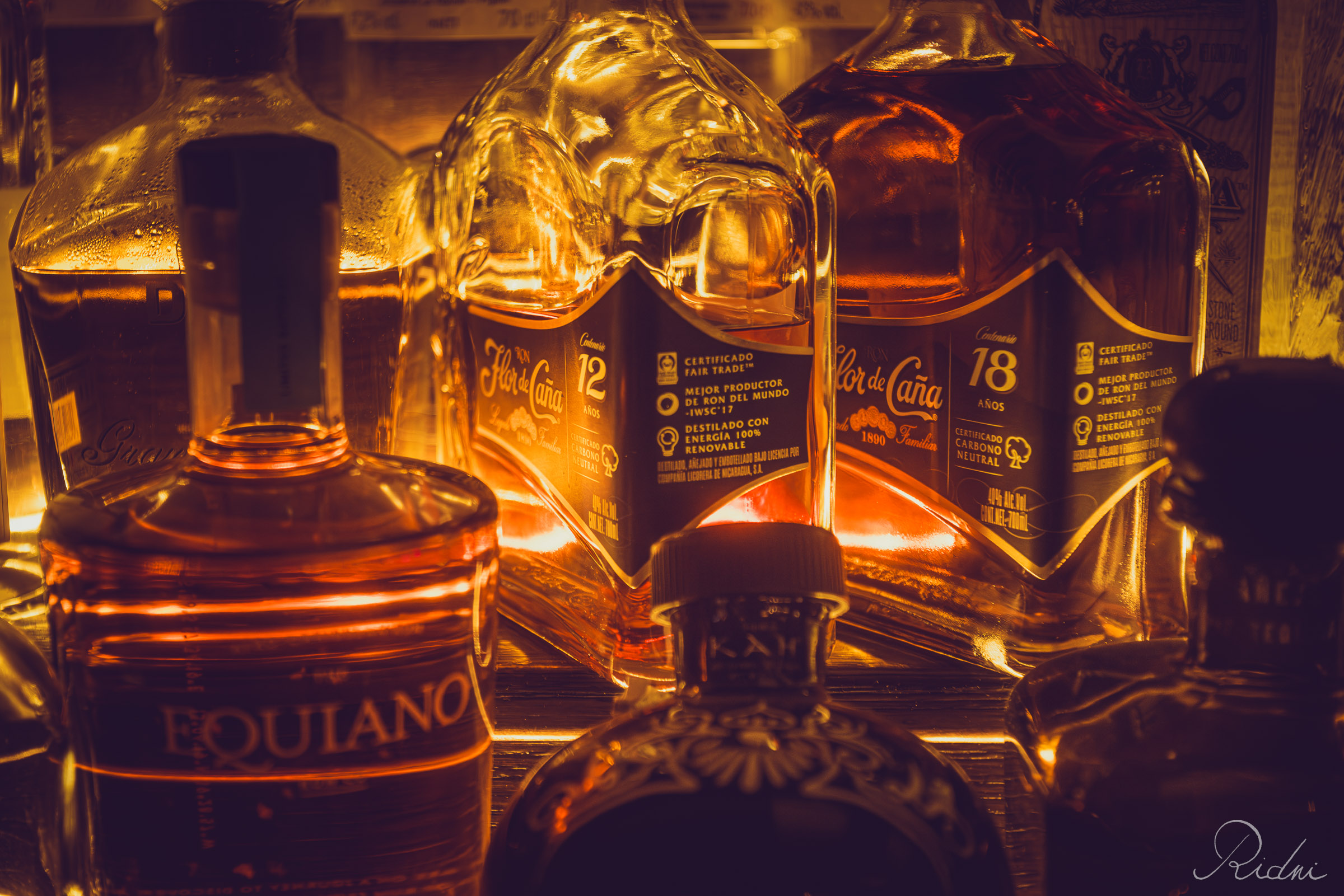 Premium rum bottles glow under warm amber lights at bar Zona in lignano, friuli.