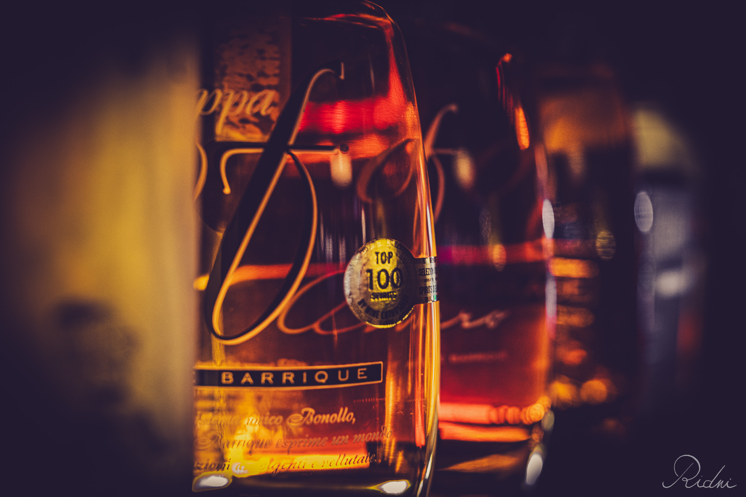 Close-up of Grappa Bonollo Barrique bottles at bar Zona in lignano, friuli, featuring warm amber lighting and elegant glass details.