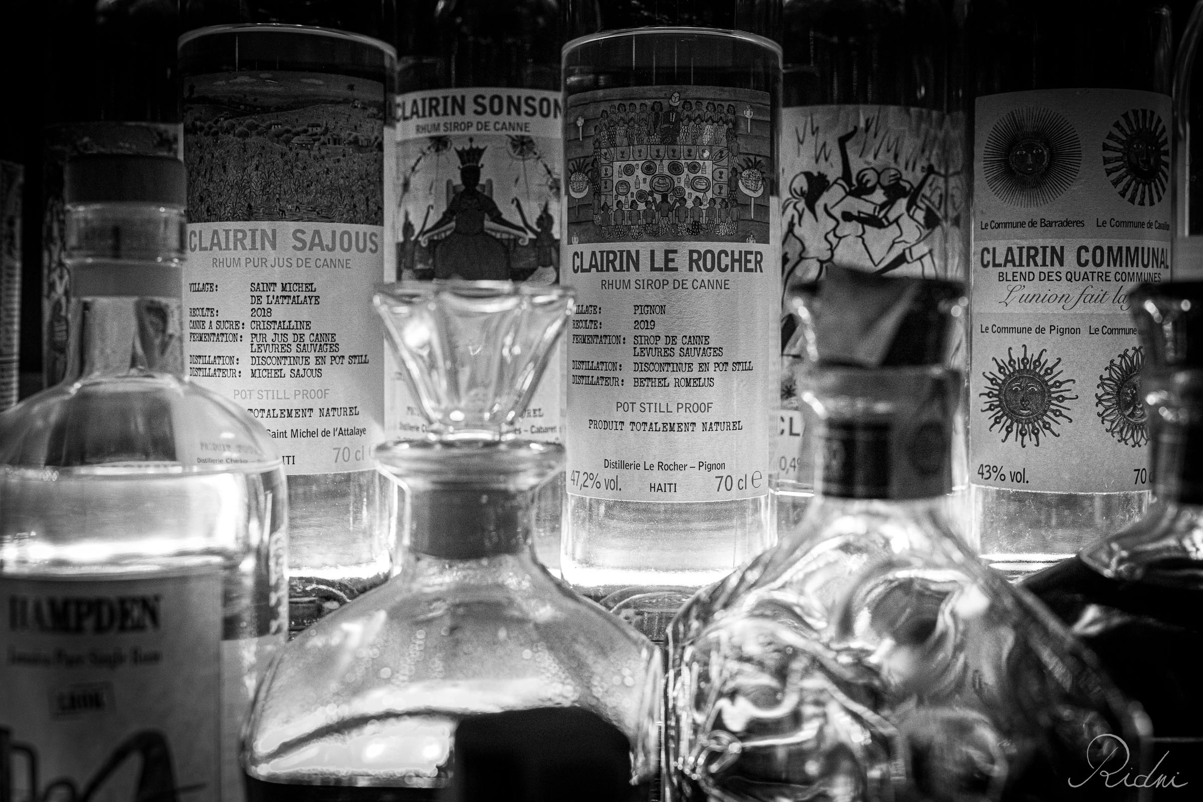 A black and white close-up of Clairin rum bottles at bar Zona in lignano, friuli, showcasing the intricate labels and textured glass.